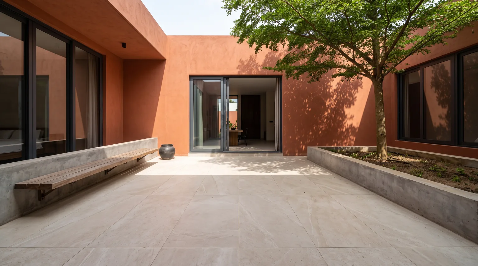 A terracotta-walled courtyard patio with a pale stone-effect porcelain floor and a young tree
