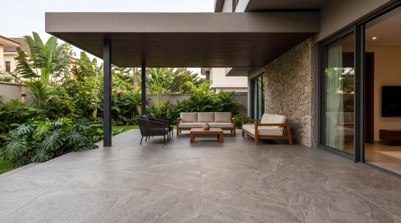 A covered terrace with a grey stone-effect porcelain floor, outdoor seating and a tropical garden
