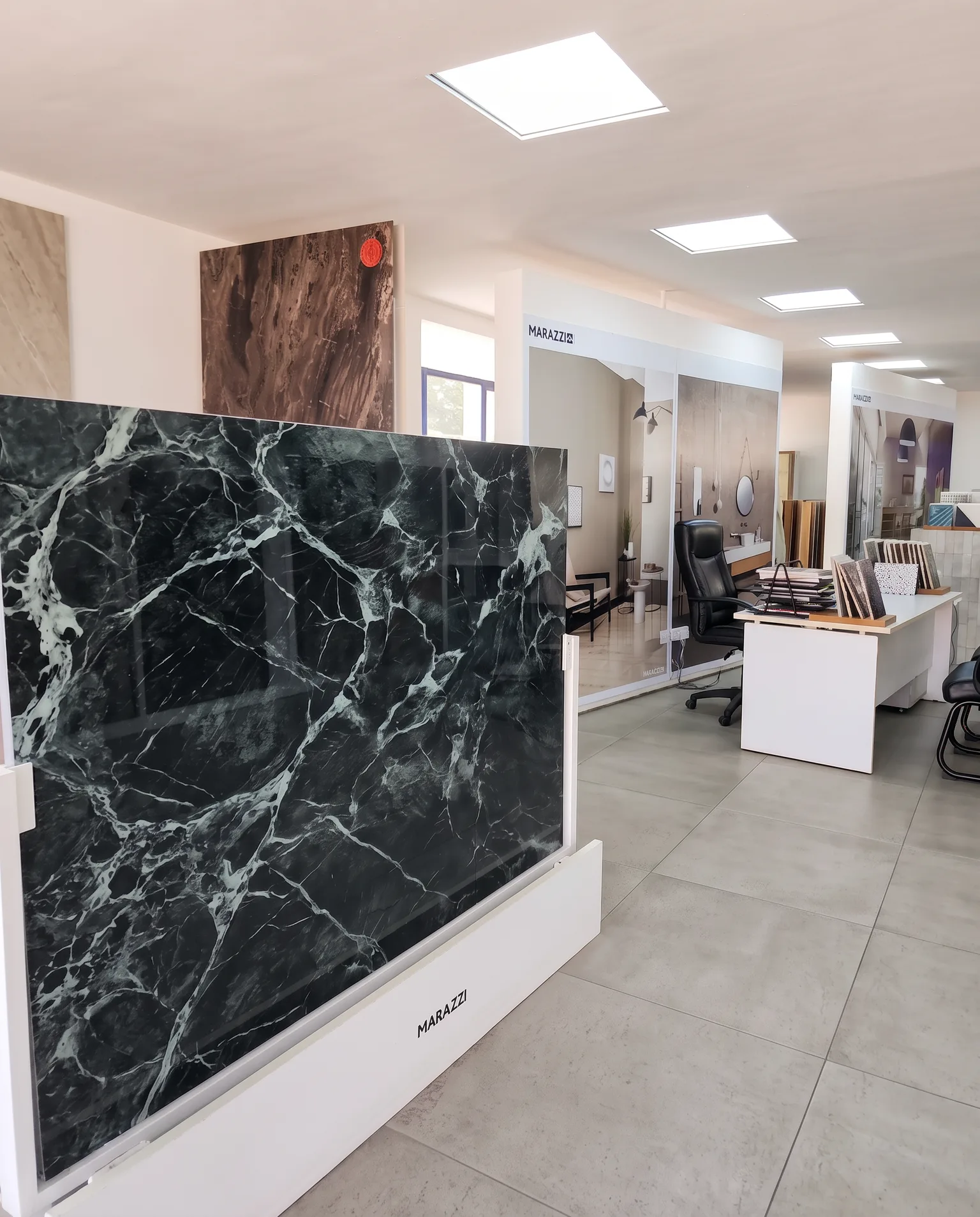 A large dark marble-effect porcelain slab on display in the showroom, with tile sample stands and a consultation desk beyond